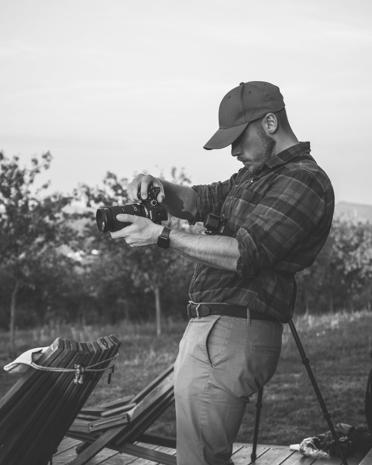 Teodor Prchlík v kšiltovce a kostkované košili nastavuje fotoaparát Sony na dřevěné terase u sadu, vedle stativ a dřevěná křesla